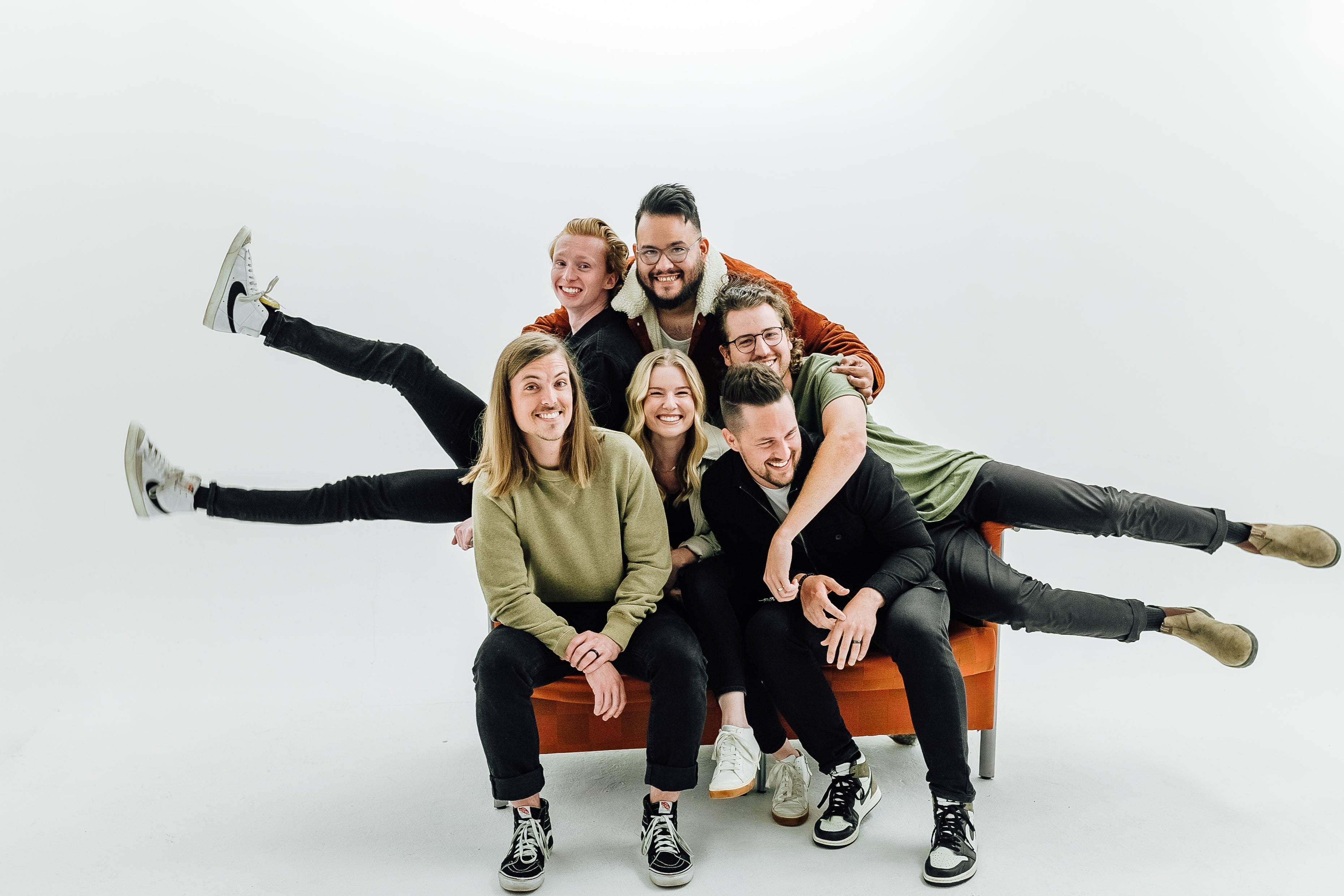 Group of six people posing on an orange couch against a white background